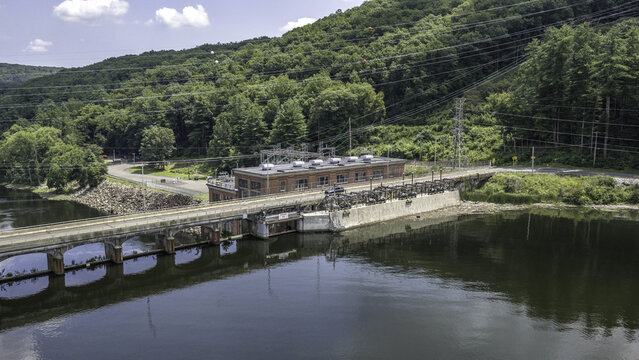Aerial view of Stevenson Generating Station hydroelectric powerhouse with brick building, switchyard, and bridge spanning the river, surrounded by green hills in Monroe, CT, United States.