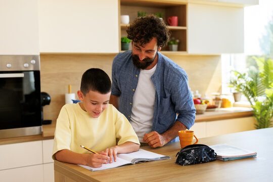 Father assisting young son with homework on kitchen counter showing family support, education, and learning at home