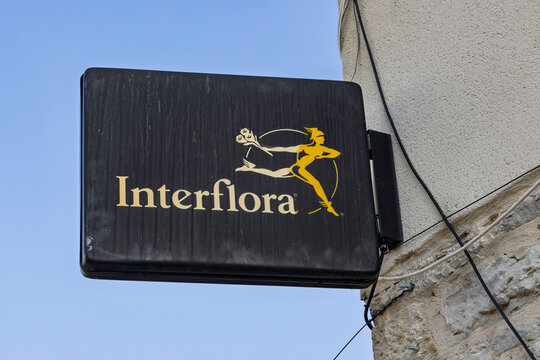 Montrevel-en-Bresse, France - July 30, 2026: Black hanging sign with gold Interflora logo and messenger icon mounted on stone building exterior.