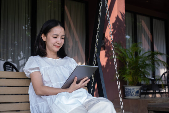 Smiling woman using a tablet while relaxing on an outdoor swing, representing remote work, digital lifestyle, online learning, productivity, wireless technology, and modern work life balance.