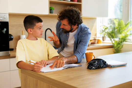 Father and son studying together at home learning and bonding over schoolwork. Dad explaining lessons to his child