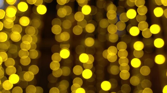 Abstract background of glowing golden yellow bokeh lights. Warm, soft-focused circular light particles twinkling out of focus.