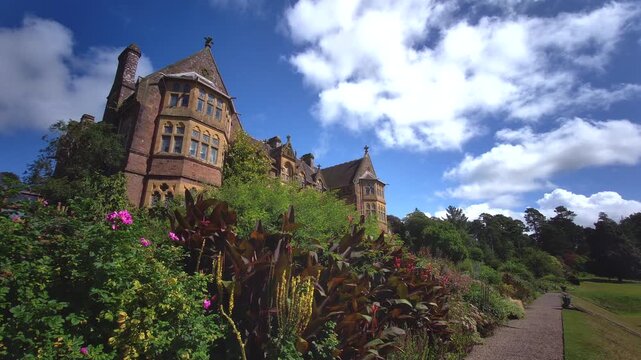 Victorian High Gothic revival facade of Knightshayes Court framed by vibrant purple flowers in the estate gardens, photographed in Tiverton, Devon, England, on 24.08.2024.