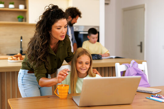 Mother and daughter using laptop for homeschooling and virtual education. Family members cooperating in a modern home environment