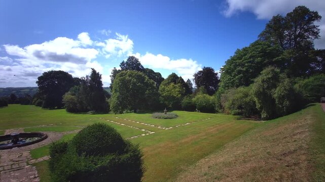 A breathtaking high-angle view overlooking a stone terrace fountain, sculpted hedges, and a grand cedar tree rolling into the Devon countryside at Knightshayes Court, UK, on 24.08.2024