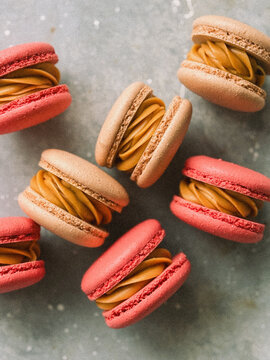 Pink French macarons filled with caramel cream on grey background top view