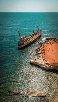 Aerial landscape view of an abandoned rusty shipwreck stranded on a rocky coastline.