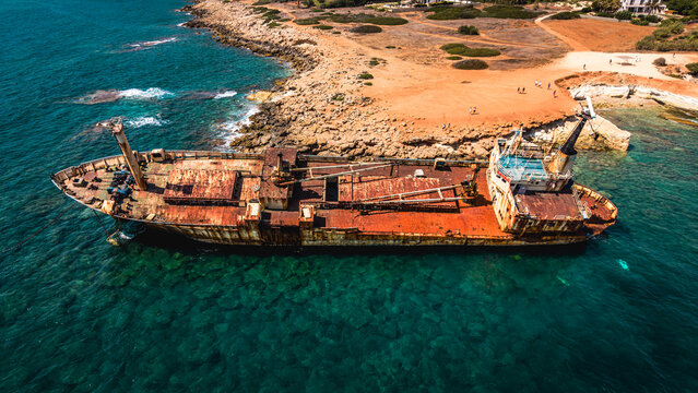 Wide aerial side view of a massive rusted shipwreck stranded in shallow waters.