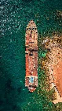Vertical top down drone shot of an abandoned rusted shipwreck in the sea.