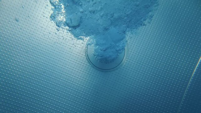 Pool jet nozzle releasing bubbles underwater on swimming pool floor
