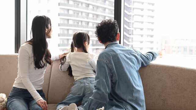 旅行先のホテルで窓の外の景色を眺める30代の日本人夫婦と6歳の子どもの後ろ姿