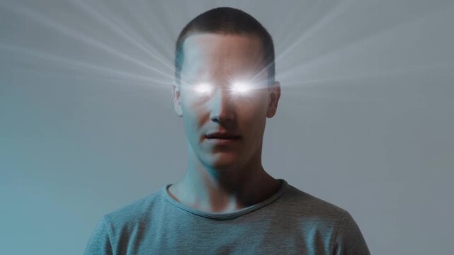 Man stands facing forward with glowing white eyes and radiating light against plain background