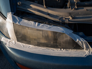 Close-up of a car headlight covered with tape around the perimeter during polishing. © Anna