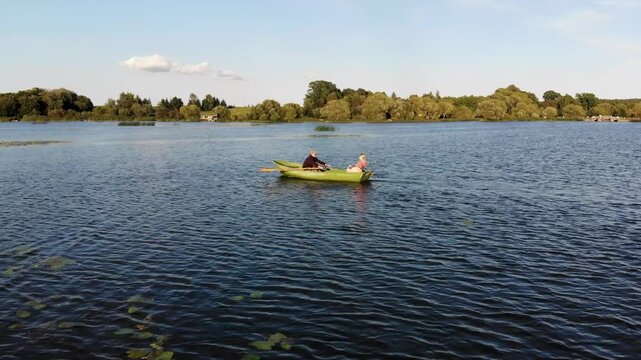 Couple rowing a boat together on a peaceful lake in the countryside at sunset
