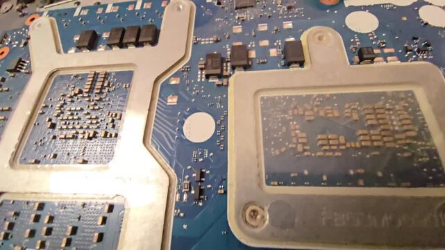 Close-up macro footage of an electronic laptop motherboard featuring metal heat sink brackets, chips, and components for computer hardware and repair concepts.