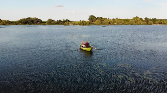 Couple rowing a boat together on a peaceful lake in the countryside at sunset