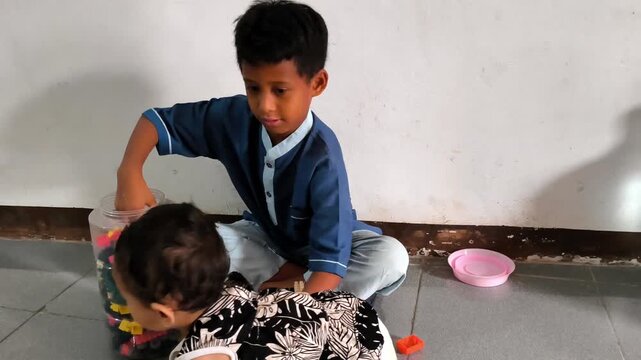A young schoolboy wearing a blue uniform plays with colorful construction blocks indoors, demonstrating concentration and creative play during childhood.
