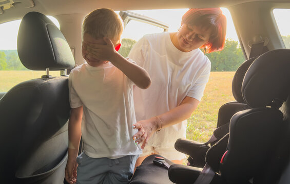 Close up of a mother's hand fastening a safety seat belt for her toddler boy in a car seat. A parent ensuring child protection and road safety during a family trip.
