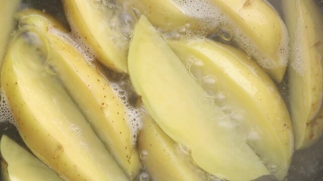 Boiling sliced potato wedges in bubbling hot water. Top view shot