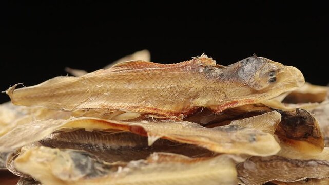 Pile of dried sole fish slowly rotating on a black background.