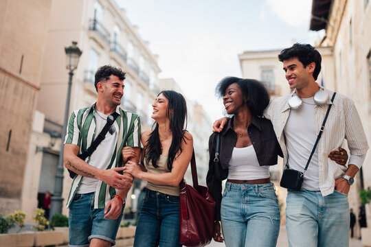 Diverse group of smiling young friends walking arm in arm, laughing and enjoying a day out on a vibrant city street
