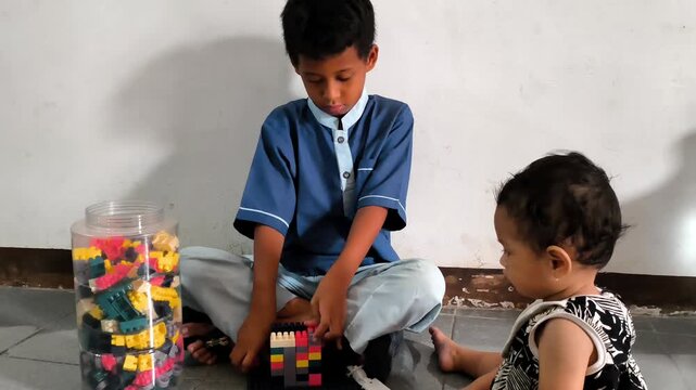 A young boy in a blue school uniform reaches toward colorful building blocks during an indoor play session, representing creativity, learning, and childhood development.
