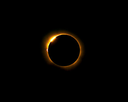 Total solar eclipse showing the diamond ring effect with solar prominences and corona visible against a dark space background during totality