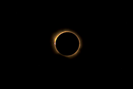 Total solar eclipse showing the diamond ring effect with solar prominences and corona visible against a dark space background during totality