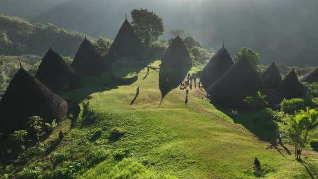 Aerial view of the traditional cone-shaped houses of Waerebo Village with people walking on the grassy clearing in Satar Mese Barat, East Nusa Tenggara, Indonesia.