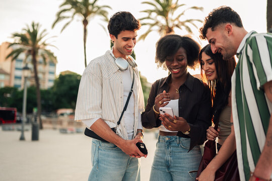 Diverse young friends enjoying social moment with phone, connecting and sharing content outdoors