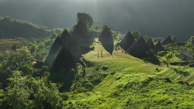 Aerial view of Waerebo Village with traditional conical houses surrounded by lush green mountains and forest in Satar Mese Barat, East Nusa Tenggara, Indonesia.