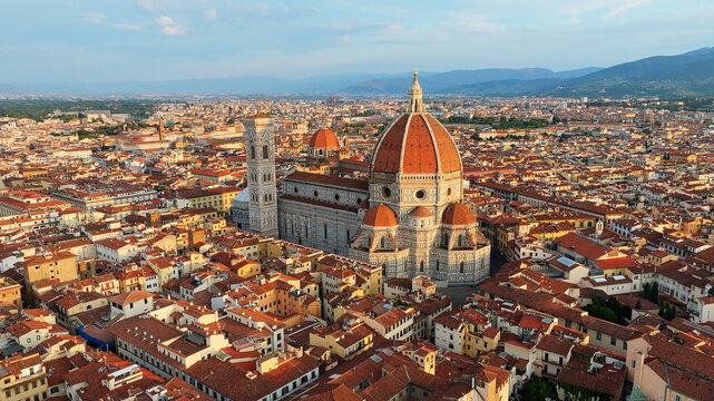 High aerial drone view of Florence Santa Maria del Fiore Duomo illuminated by early morning sun with surrounding terracotta roofs and Tuscan hills summer Italy