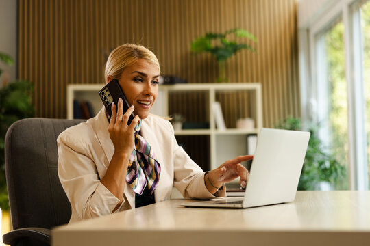 Businesswoman engaged in a phone call while working on a laptop in a modern office