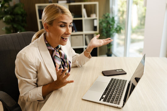 Engaged businesswoman in a small office, communicating via laptop with enthusiasm