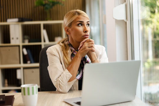 Bright small office with a thoughtful businesswoman contemplating at her desk