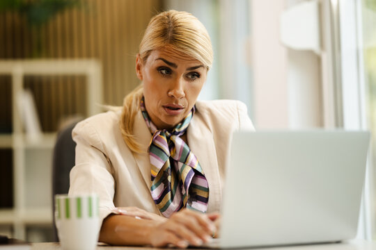 Bright small office with focused woman working on laptop, wearing stylish scarf
