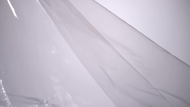 Transparent plastic film forms glossy silver folds and soft reflections on an abstract surface. Concept packaging, material texture, banners, websites and advertising design.