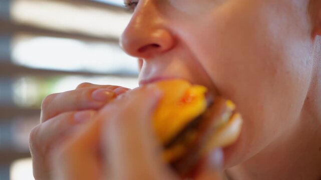 Close-up of woman taking a bite of hamburger and enjoying fast food. Appetite, food craving, indulgent eating, comfort food and casual restaurant experience concept.