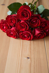 Fototapeta premium Bouquet of fresh red roses with green leaves on a light wooden table, romantic floral gift for special occasions