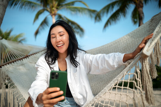 Asian woman embracing freedom at the beach, enjoying travel, self-expression, and digital connection