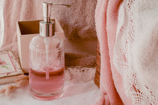 Pink liquid soap dispenser creating bubbles, symbolizing cleanliness, beauty, skincare, and luxury, with soft pink towels and white lace for a serene self care and wellness experience