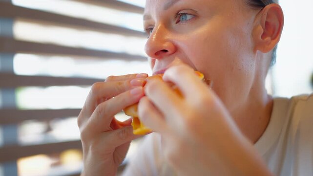 Close-up of hungry woman biting into a juicy cheeseburger at a cafe. Fast food meal, burger, casual dining, food enjoyment and indulgent eating concept.