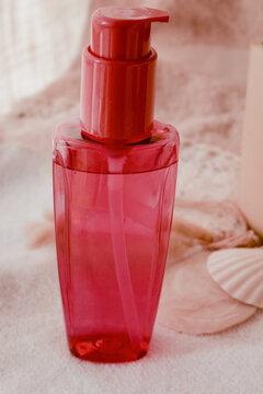 Pink pump bottle standing on a white towel with seashells, containing a transparent cosmetic liquid for personal wellness and beauty treatments