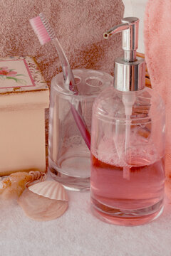 Pink toiletries and a toothbrush in a holder, accompanied by a decorative box and seashells, creating a calm scene for wellness, oral hygiene, and beauty routines on white and pink towels
