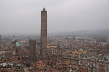 Fototapeta premium Aerial view of the iconic Two Towers of Bologna, Torre Asinelli and Torre Garisenda, rising above the historic cityscape on a misty winter day, Italy.