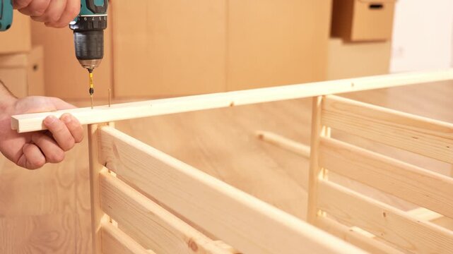 Assembling a wooden shelving structure using a screwdriver. A man uses screws to fasten two parts of a wooden shelving unit together. Furniture assembly tool