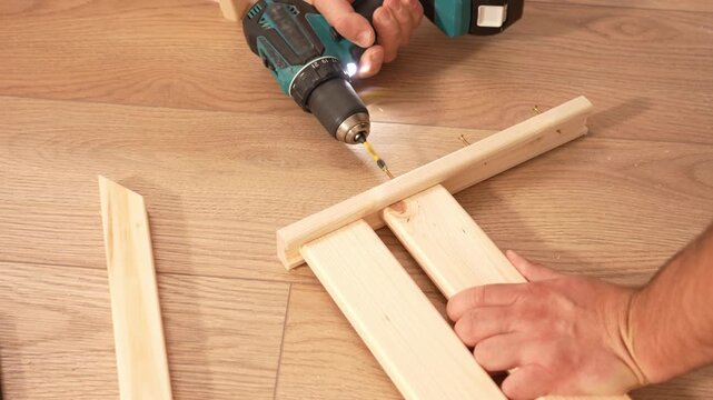 Assembling a wooden shelving structure using a screwdriver. A man uses screws to fasten two parts of a wooden shelving unit together. Furniture assembly tool