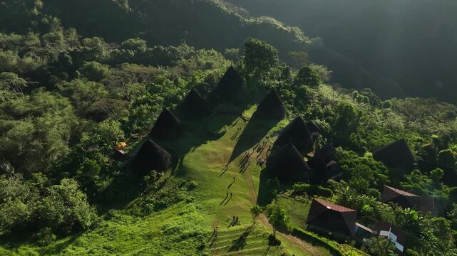 Aerial view of Waerebo Village with its iconic conical houses surrounded by lush green mountains and forest in Satar Mese Barat, East Nusa Tenggara, Indonesia.