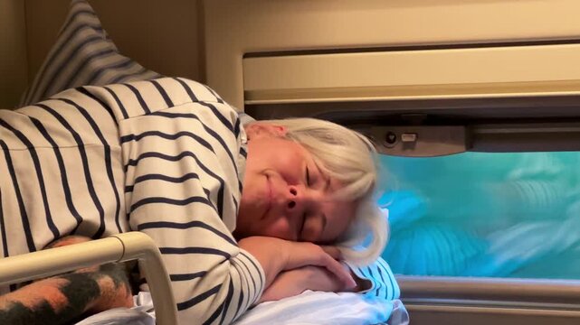 An adult woman resting with her eyes closed on the upper berth in a train carriage, travel agency, tourism industry, vacation journey, railway relaxation.