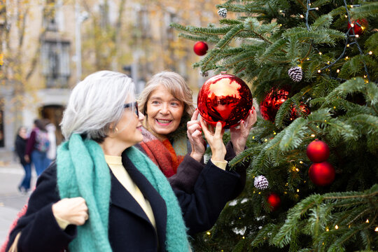 Senior women friends decorating outdoor christmas tree